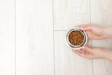 Woman with bowl of dry pet food on floor at home, top view. Space for text