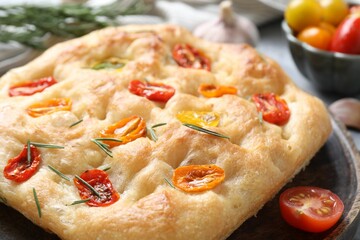 Delicious focaccia with tomatoes and rosemary on table, closeup