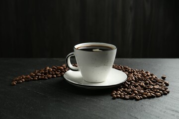 Aromatic coffee in cup and beans on black table