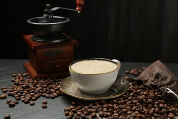 Aromatic coffee in cup, beans and grinder on black table