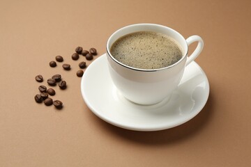 Aromatic coffee in cup and beans on beige background, closeup