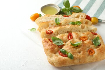 Cut delicious focaccia with tomatoes, basil and oil on light table, closeup. Space for text