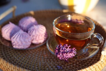 Beautiful lilac flowers, tea and zephyrs on table in garden, closeup