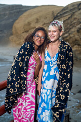 Two smiling young women leaving beach at sunset wrapped in towels