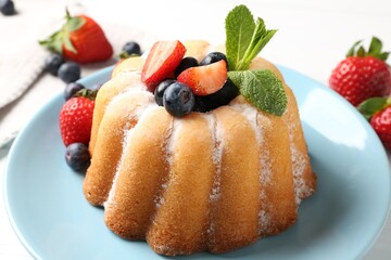 Tasty Bundt cake with powdered sugar and berries on white table, closeup