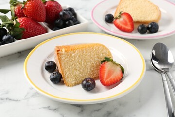 Pieces of tasty bundt cake with berries on white marble table, closeup