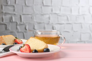 Pieces of tasty bundt cake with berries and tea on pink wooden table, closeup. Space for text