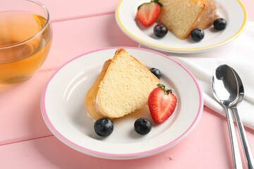 Pieces of tasty bundt cake with berries and tea on pink wooden table, closeup