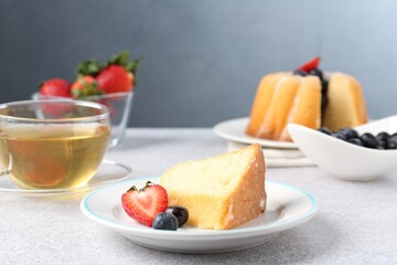 Piece of tasty bundt cake with berries and tea on light grey table, closeup
