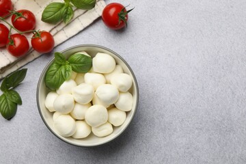 Tasty mozzarella cheese balls, tomatoes and basil on light grey table, flat lay. Space for text