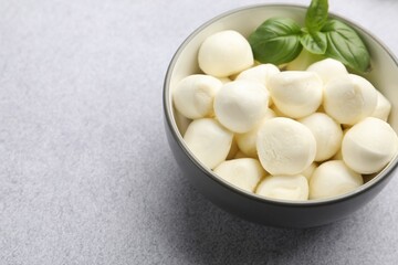 Tasty mozzarella cheese balls and basil on light grey table, closeup. Space for text