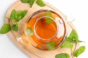 Aromatic lemon balm tea in glass teapot and fresh leaves on white table, top view