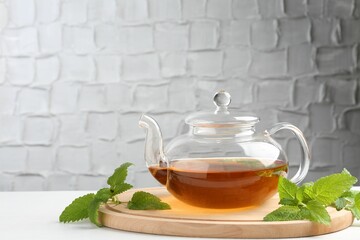 Aromatic lemon balm tea in glass teapot and fresh leaves on white table against light background,...