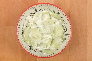 A bowl of creamy cucumber salad with sour cream, garlic, and dill is presented on a wooden surface