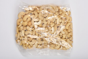 A clear plastic bag filled with cashew nuts is displayed on a white surface