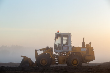 Construction machinery in the rays of the rising sun, early morning at the construction site