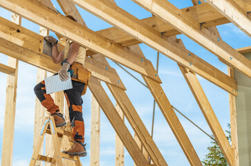 Construction Worker on Ladder Assembling Wooden Beams in Bright Daylight During Home Renovation Project