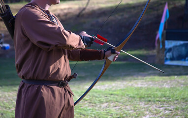Archer in historical costume aims longbow at a target during a Medieval Fair during a local...