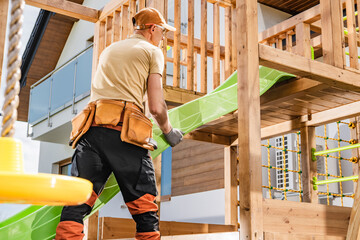 Man Installing a Green Slide in a Wooden Playground Structure During Daylight at a Residential Backyard