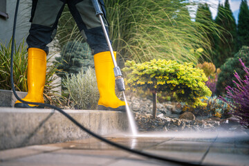 Gardener Using Pressure Washer to Clean Stone Patio in Vibrant Landscape During Sunny Day