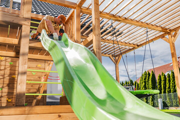 Construction of a Vibrant Green Slide on a Wooden Play Structure in a Backyard During Sunny Weather...