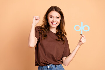 Happy woman in casual attire with brown shirt holding a blue symbol with confident gesture against beige background