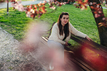 Woman sitting on a bench in a park surrounded by blooming flowers during a sunny day in spring