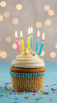 A single cupcake with white frosting and several lit candles on a blue surface with sprinkles