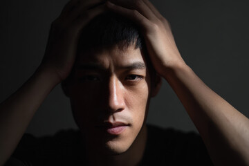 Man looking distressed and holding his head in dark, quiet setting with dramatic lighting emphasizing his emotional expression