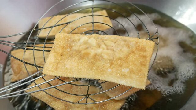 Close up of fried pastry being lifted from hot oil with a metal strainer in a kitchen setting