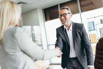 Mature businessman and colleague shaking hands in a modern office symbolizing partnership and corporate teamwork