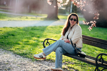 Woman sitting on a park bench enjoying a sunny day surrounded by blooming trees in spring