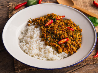 Rice topped with stir fried pork with yellow curry paste in white plate on wooden table background. Traditional Thai southern food