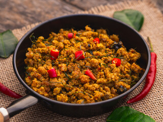 Stir fried pork with yellow curry paste in mini pan on wooden table background. Traditional Thai southern food