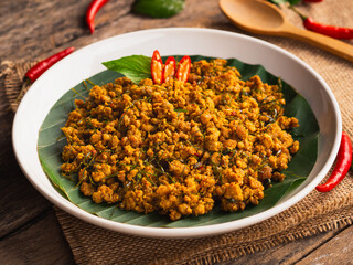 Stir fried pork with yellow curry paste in white plate on wooden table background. Traditional Thai southern food