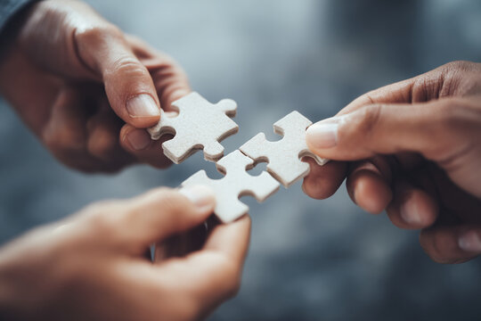 Close-up of three hands connecting puzzle pieces, symbolizing teamwork, collaboration, and problem-solving in business