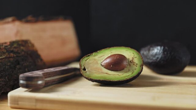 Hand placing a sliced ​​avocado on a wooden chopping board