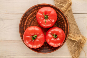 Three pink tomatoes with a clay plate on a wooden table, close-up, top view.
