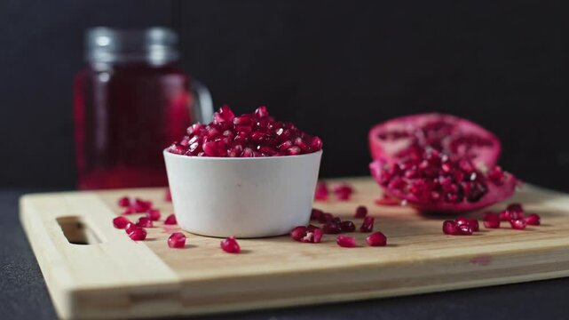 Ceramic bowl full of pomegranate and cutted pomegranate with seeds lie on a wooden cutting board on the concrete background