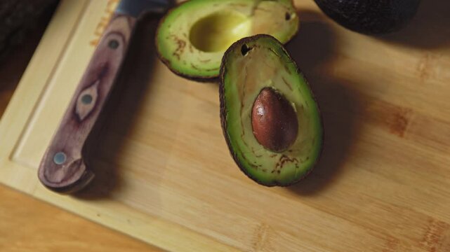 Three avocados and knife lie on the wooden cutting board. View from the top