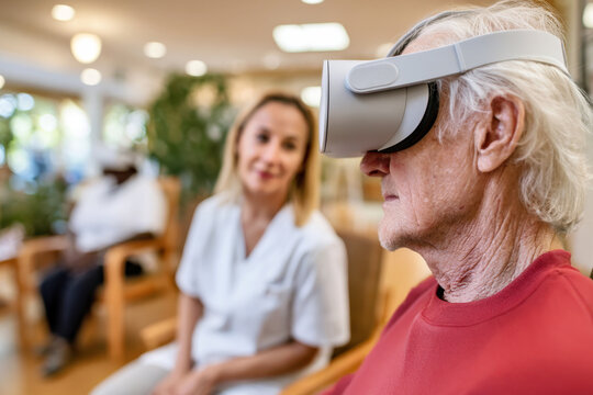 Healthcare worker and elderly man with VR headset in nursing home. Therapeutic sessions using modern technology. Seniors with VR glasses enjoy new and engaging experience