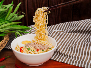 Use chopsticks to pick up instant noodle soup with minced pork and half boiled egg in white bowl on...