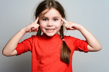 Smiling girl in red shirt playfully touches her temples.