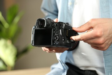 Man inserting SD memory card into photo camera indoors, closeup