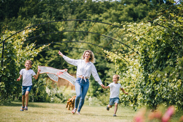 Fototapeta premium Mother and sons flying a kite. Happy Family day. Family flying a kite in a clearing near the forest.