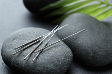 Acupuncture needles, spa stones and leaves on grey background, closeup