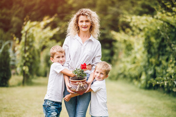 Two young sons help their mother plant flowers in flowerpots. Gardening Day, planting flowers. Mom...