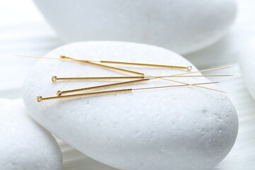 Acupuncture needles and spa stones on white wooden table, closeup