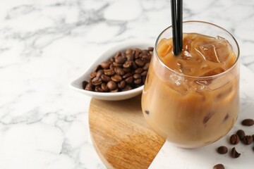 Tasty iced coffee and beans on white marble table, closeup. Space for text