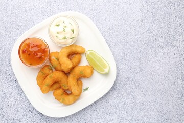 Tasty tempura shrimps, lime and sauces on grey textured table, top view. Space for text
